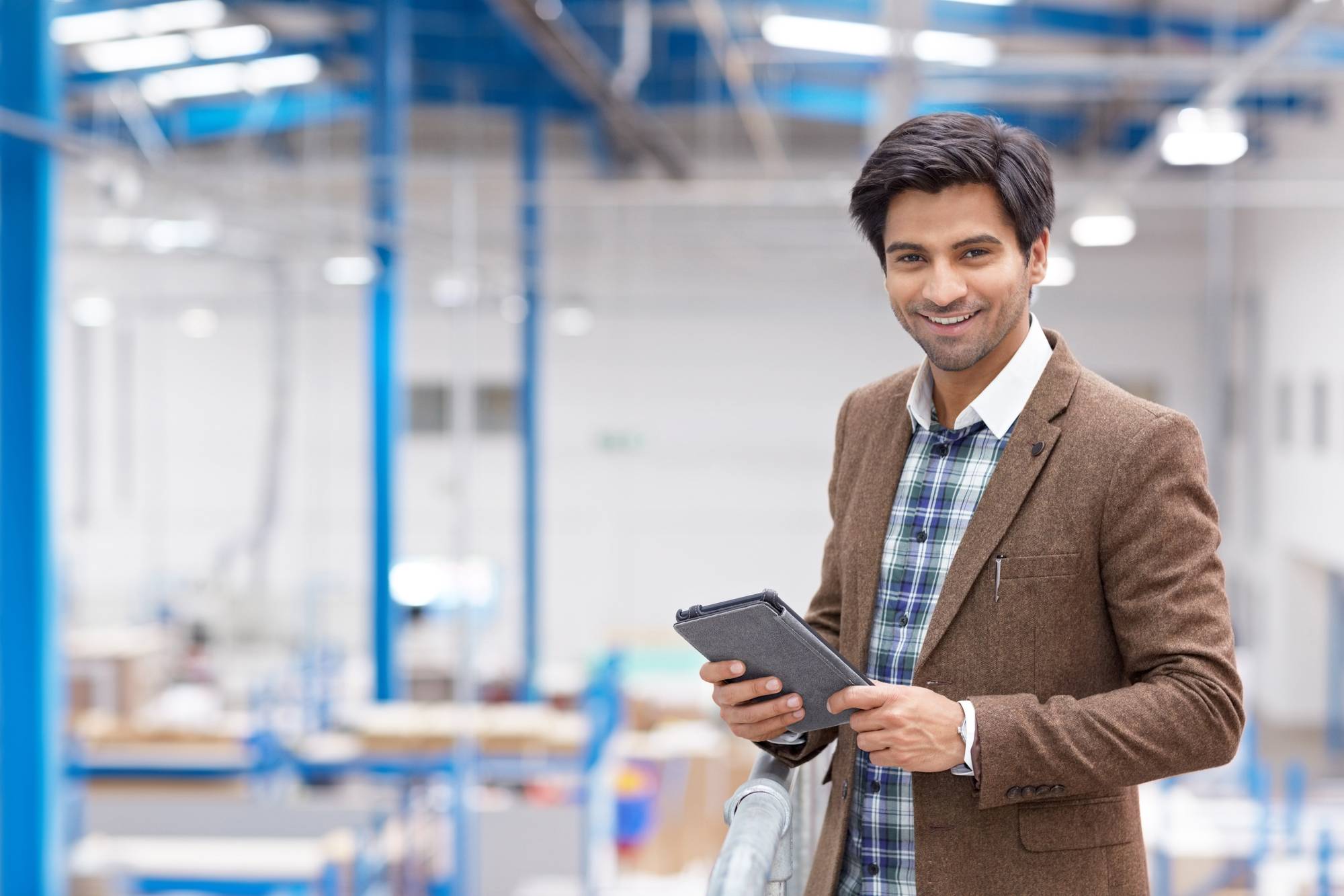 Smiling businessman with a tablet in a modern manufacturing plant.