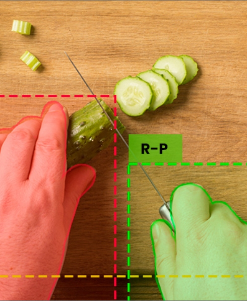 One hand holds a cucumber, another cuts it with a knife. Machine vision highlights danger zones.