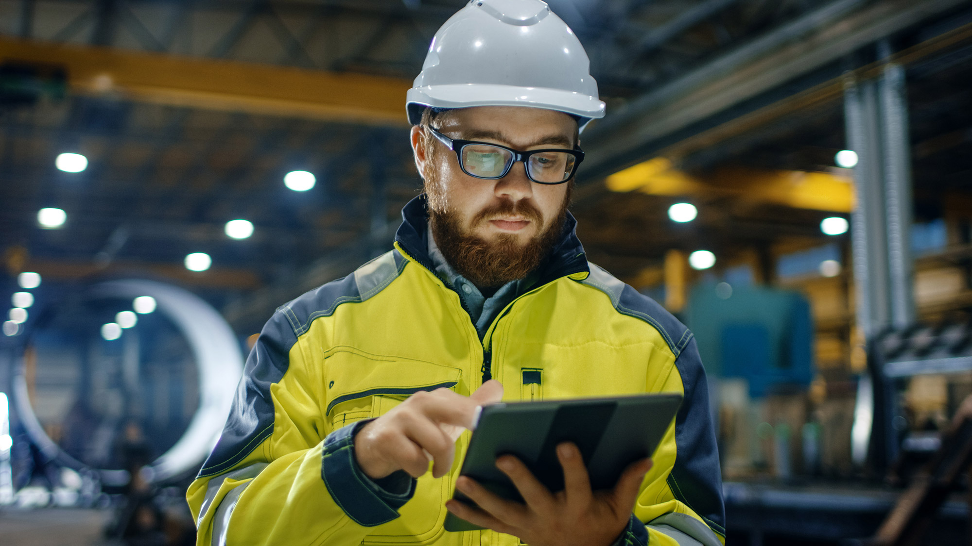 Construction worker in high-visibility jacket using a tablet on the factory floor.